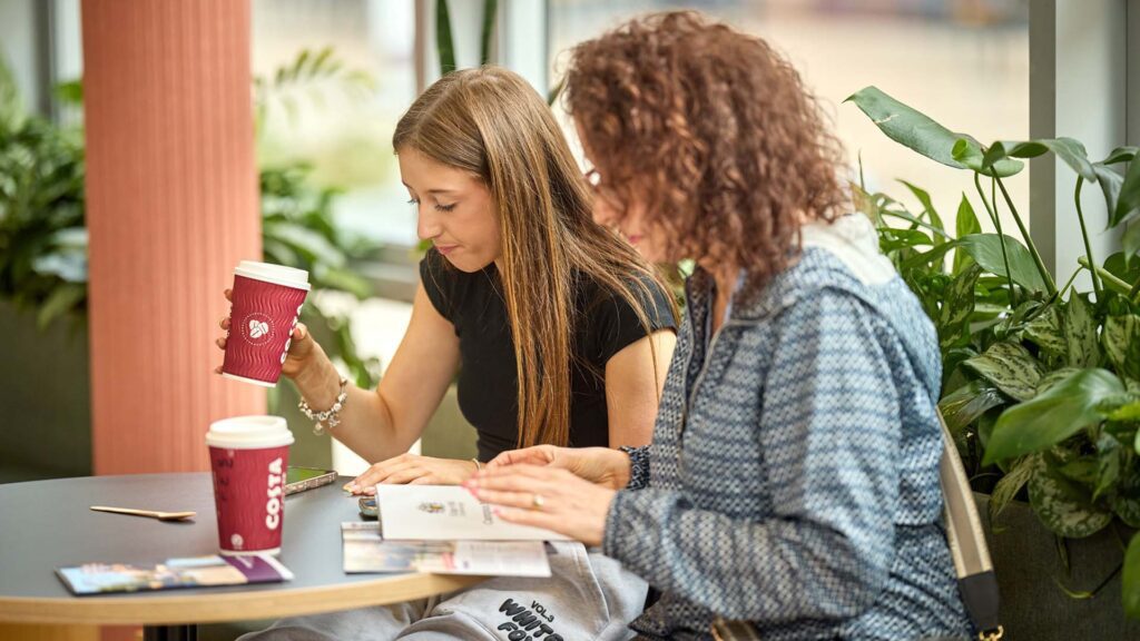 Image of visitor with their parent/supporter in the Hub reading materials at an open day