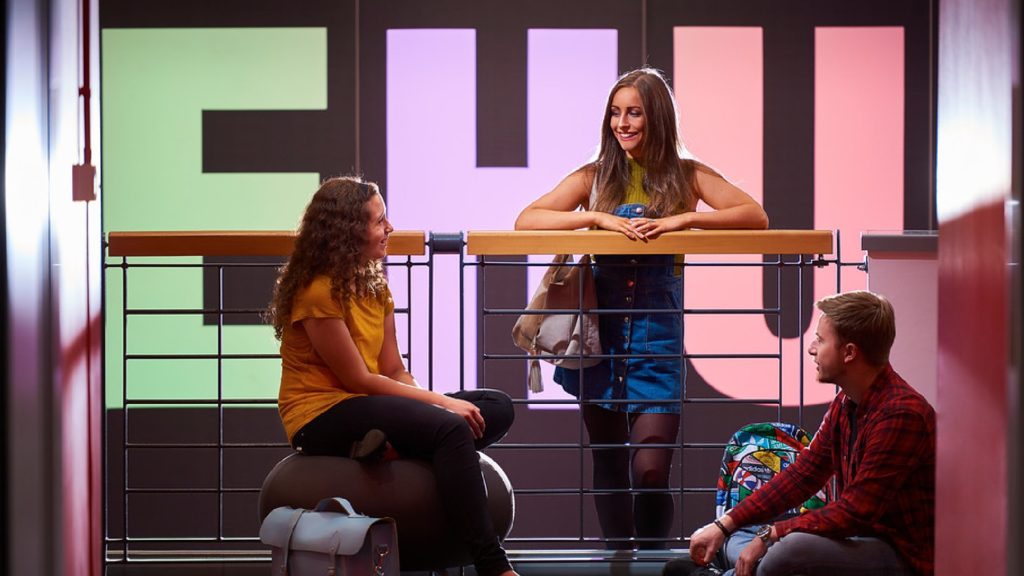Three people are talking inside the arts centre at Edge Hill.