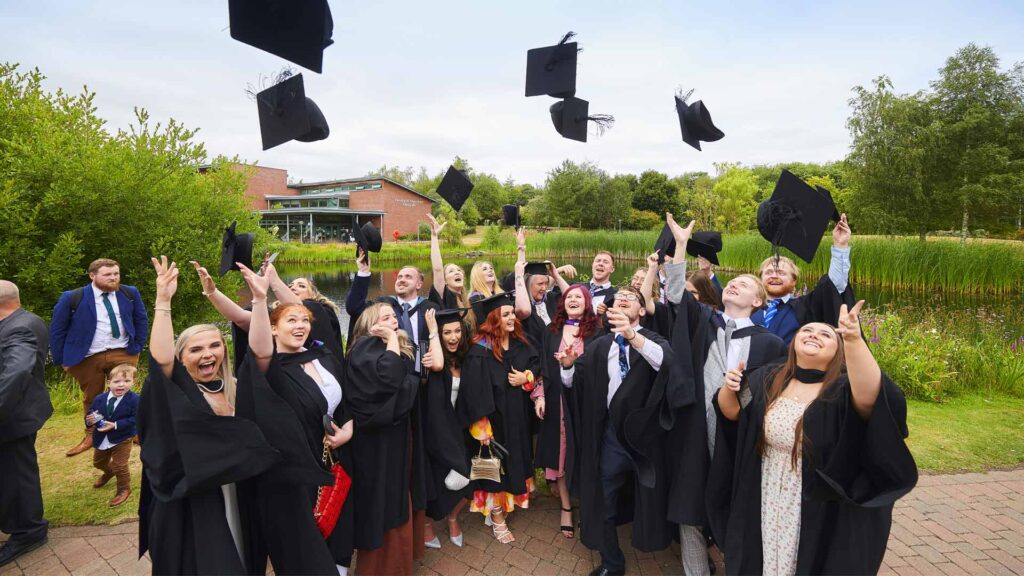A group of graduates throwing their mortar boards in the air after a 2022 Edge Hill graduation ceremony