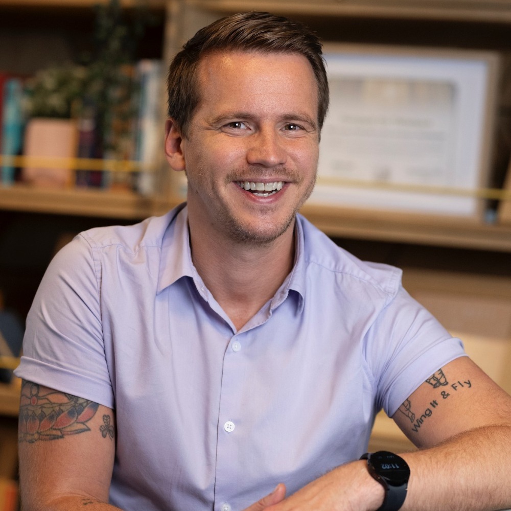 portrait of Jake Mills wearing blue short sleeved shirt, smiling at the camera. 