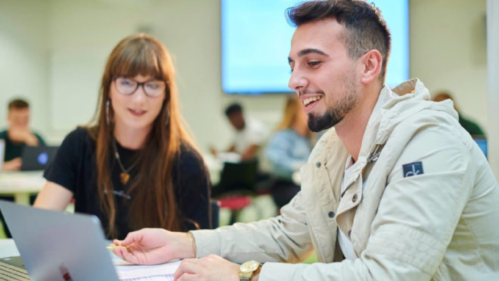 Two students are looking at a laptop.