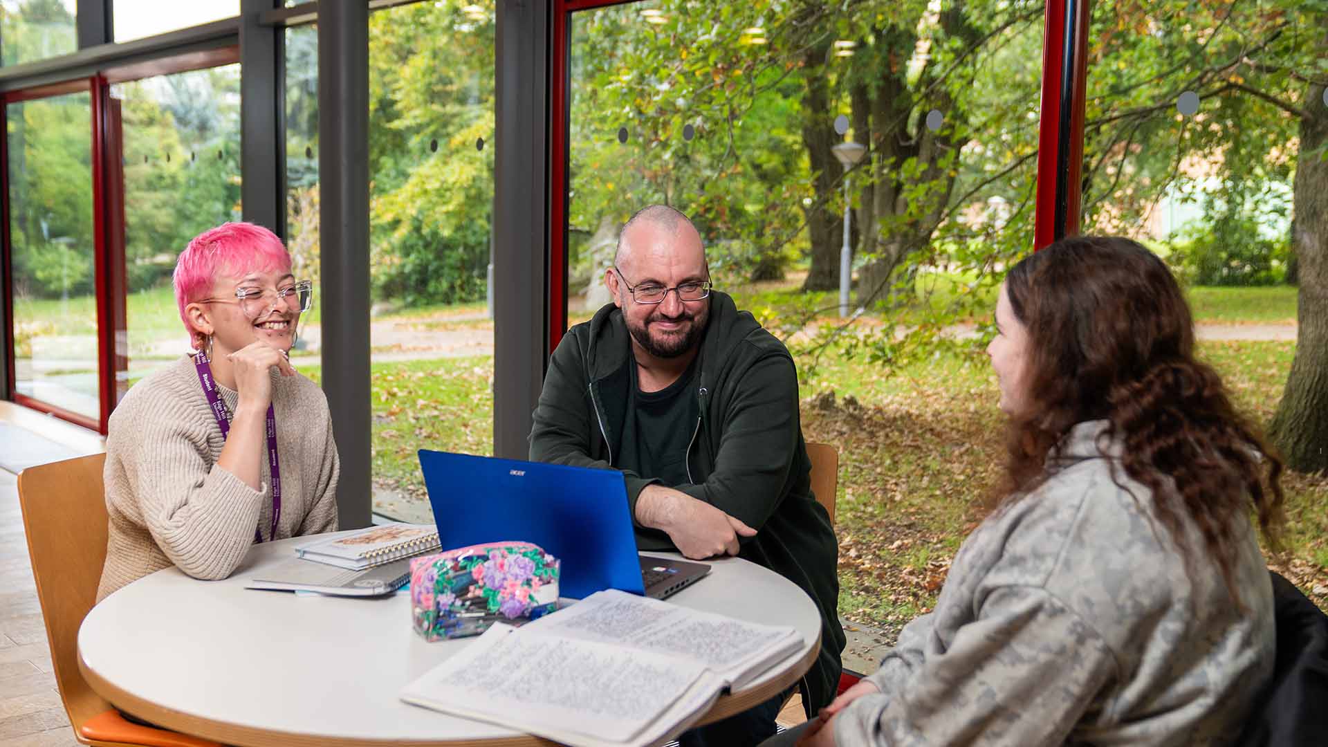 Three students sat around a table with a laptop and notepad