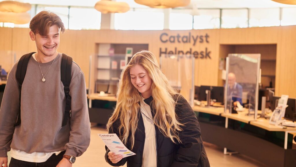 Two students walking away smiling from the Catalyst Helpdesk holding a brochure with information
