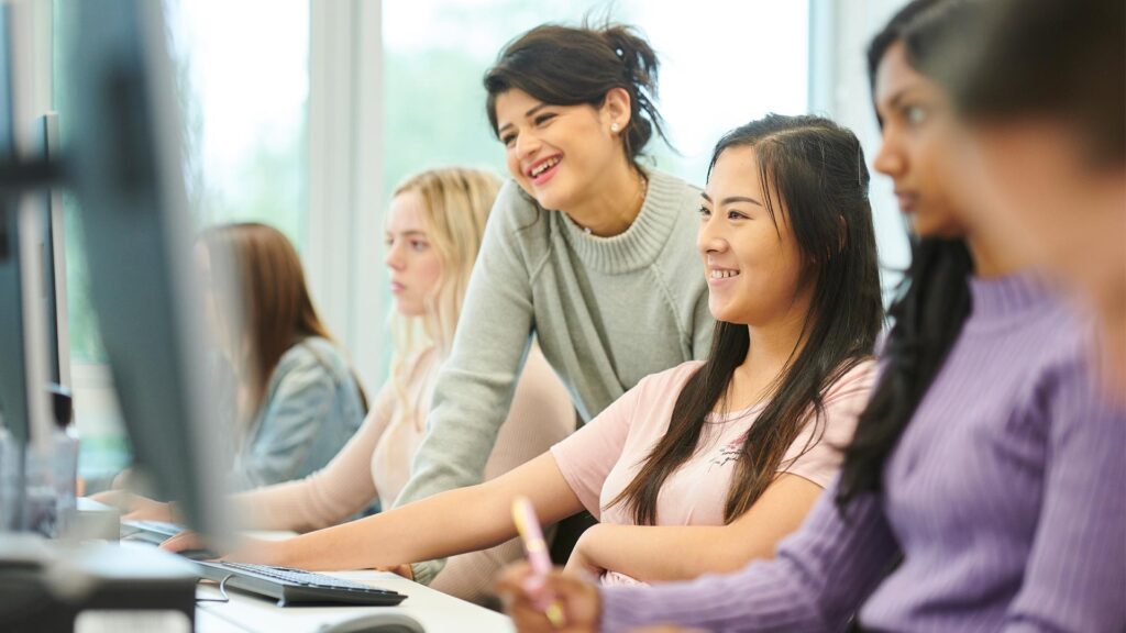 Students working on computer in tutorial session while tutor helps to guide them
